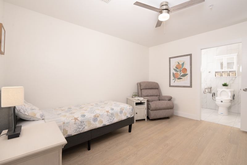 Resident bedroom with a recliner, reading lamp and private bathroom beyond
