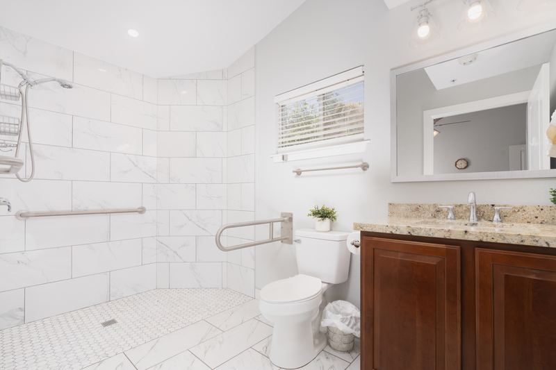 Bathroom with a tiled walk-in shower, grab bars and a wood vanity