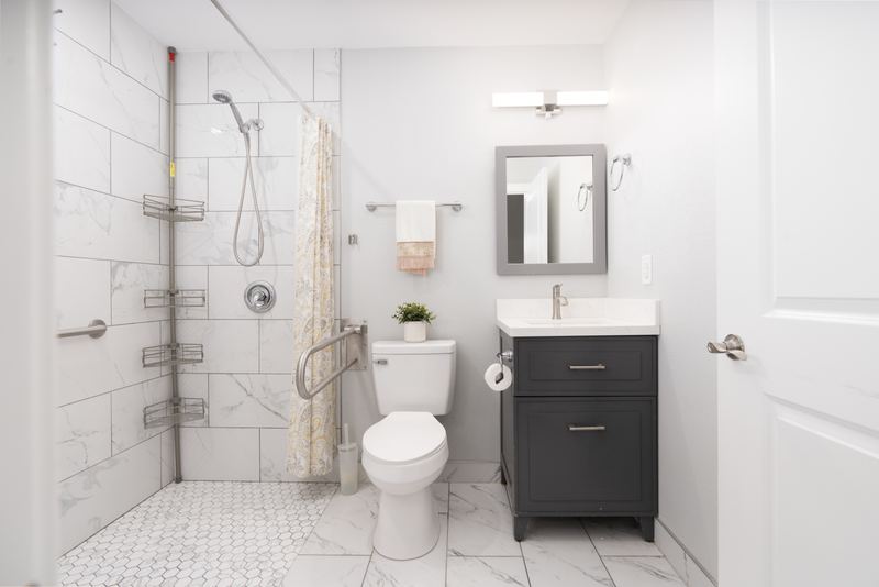 Bathroom with a curtained walk-in shower, grab bars and a grey vanity