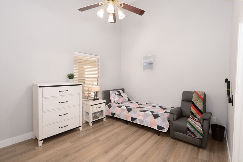Bedroom with a dresser, armchair and a grab bar beside the bed