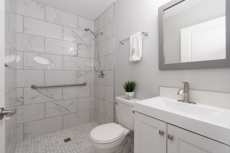 Bathroom with a tiled walk-in shower, grab bars and a white vanity