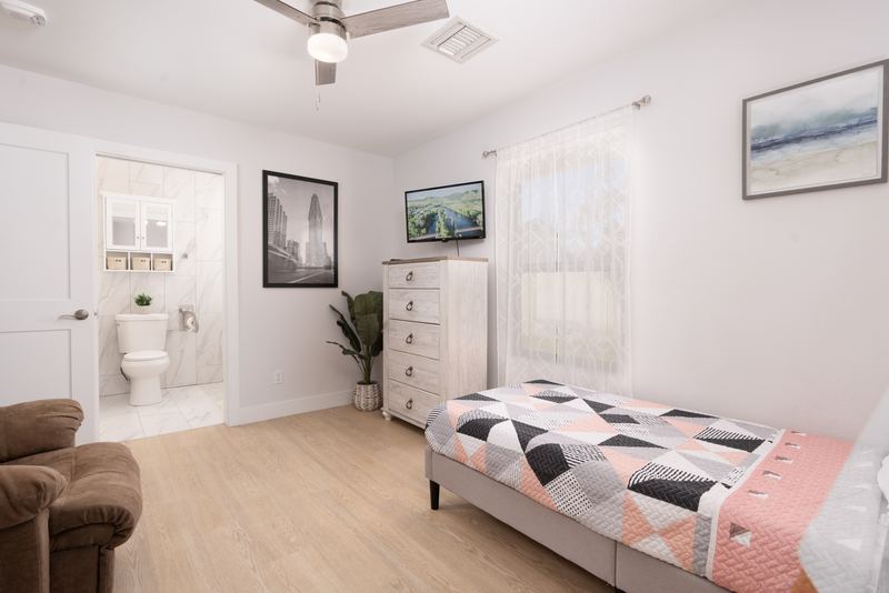 Bedroom with a recliner, dresser and a private bathroom through the doorway